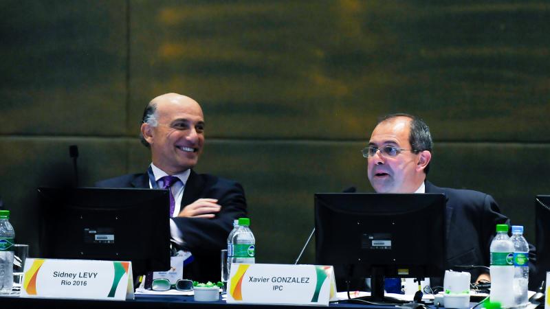 Picture of IPC Chief Executive Xavier Gonzalez and his Rio 2016 counterpart Sidney Levy dressed in suits seated behind two microphones on a table in a formal meeting.