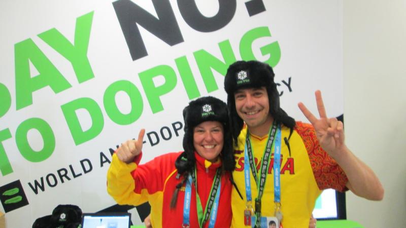 Two people give a thumbs up and a peace sign in front of a "Say No! to Doping" sign.