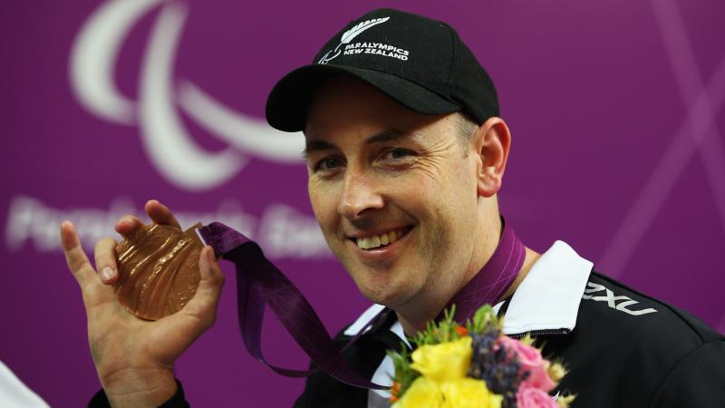 Portrait of smiling man wearing a basecap showing his bronze medal to the camera.