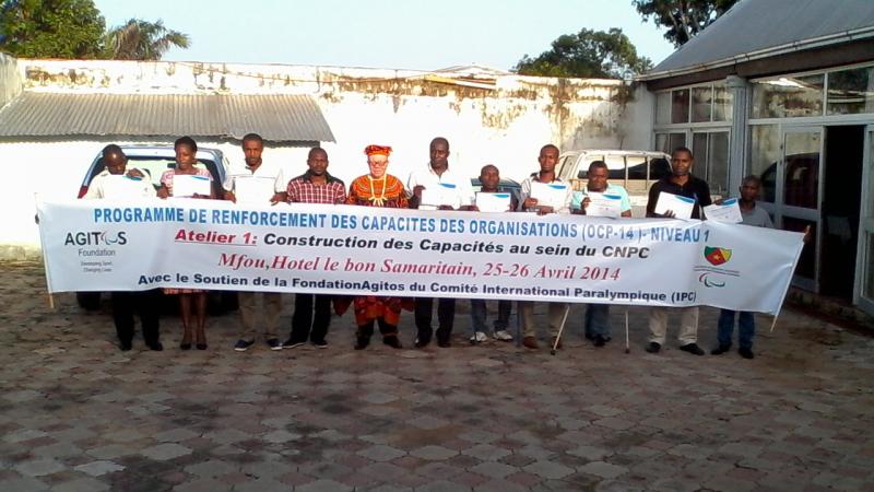 A group shot of people standing and sitting in wheelchairs behind a banner with the following text: Programme de renforcement des capacites des organisations - Niveau 1