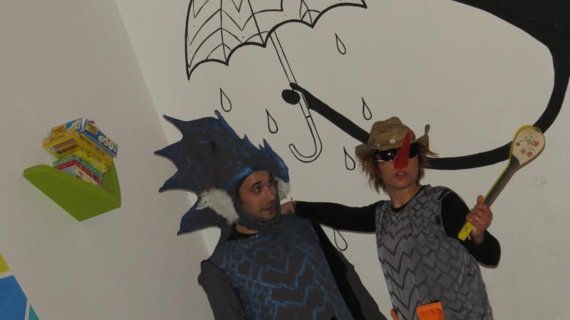 Two persons with a dragon costume stand in front of a wall. An umbrella is painted on the wall behind.