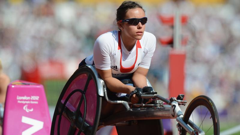 A female wheelchair racer leans forward in her chair wearing sunglasses