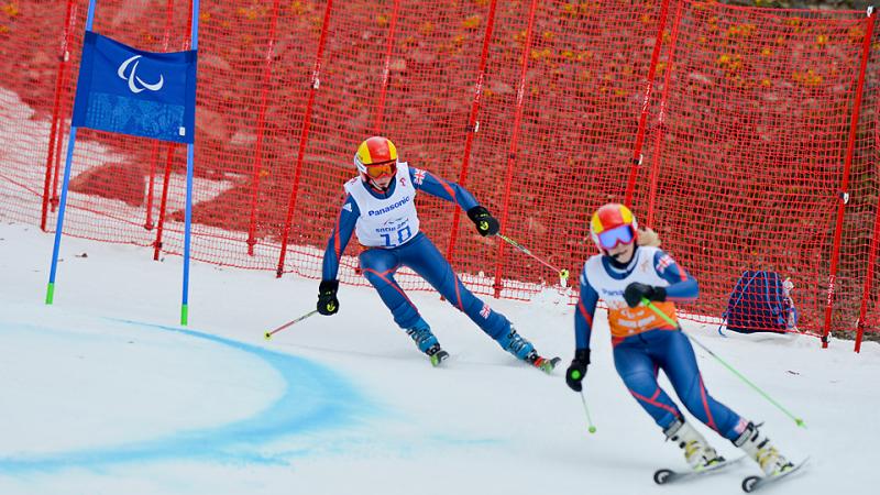 Two skiers in race suits going down a slope