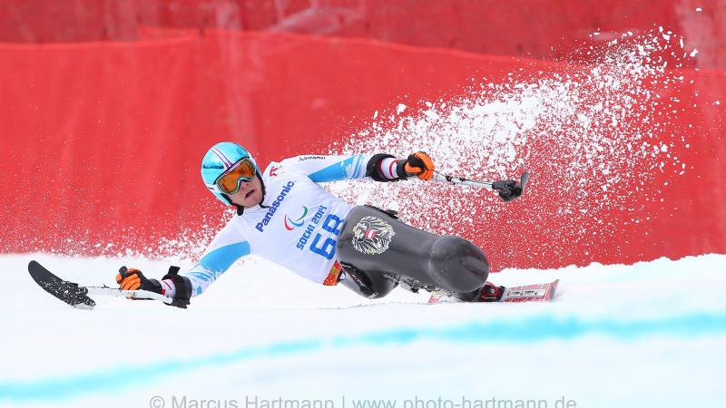 Sit skier Roman Rabl rounds a turn very low, at speed with snow spraying behind him and outriggers outstretched.