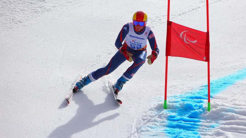 Skier in navy and white ski suit and red helmet skis past a giant slalom gate