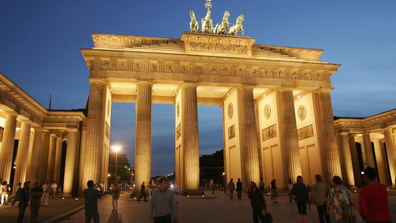 Illuminated gate in twilight. People passing by in front of the gate