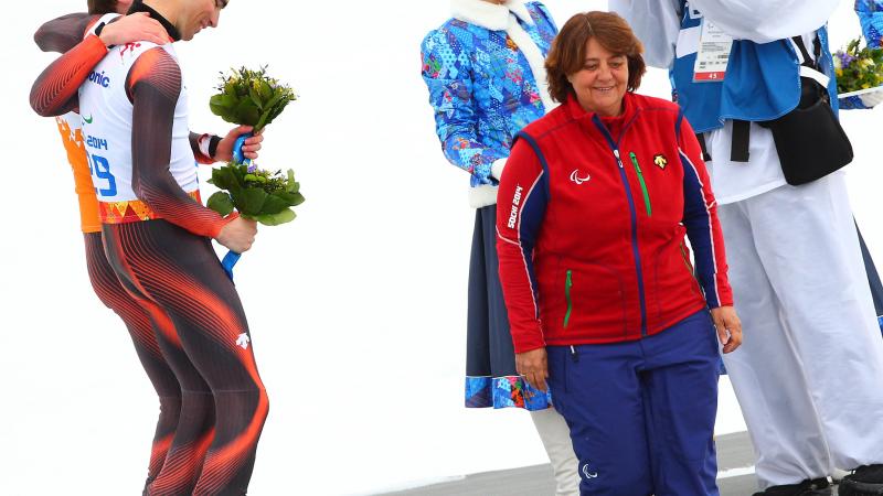 Two skiers on a podium with a women presenting them their medals