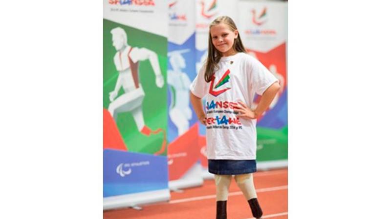 A young amputee girl smiles to the camera, wearing a white t-shirt with a Swansea 2014 imprint