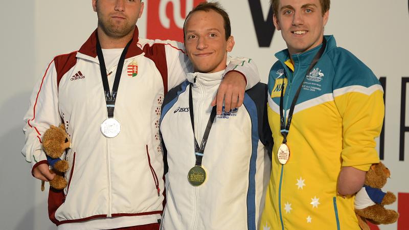 Three swimmers in their team dresses on the podium wearing medals, putting their arms around each other