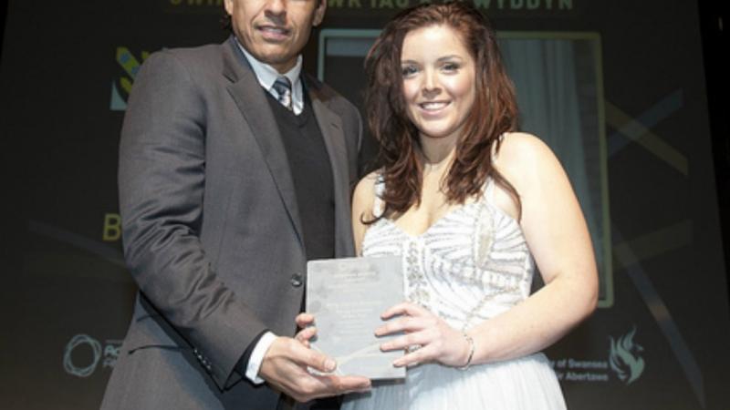 Women and men in dress and suit both hold an award and smile to the camera