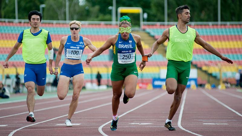 Two blindfolded women running on a track with their male guides. All wearing running suits