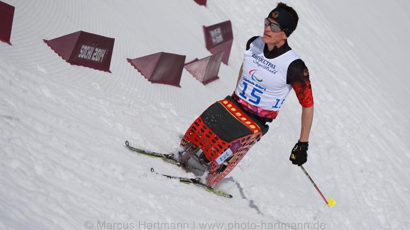 A sit skier rounds a bend in the course in the stadium in Sochi, pushing forward at speed.