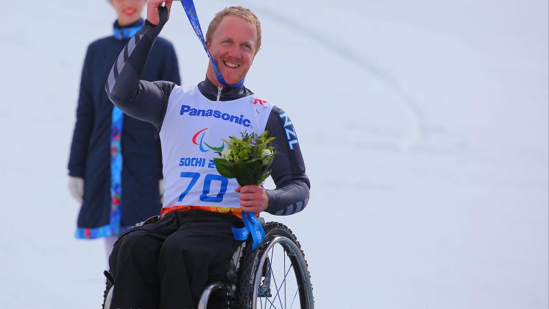 Man in wheelchair on a podium, holding his medal