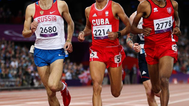 Four runners dressed in shorts and vest competing on a red athletics track.