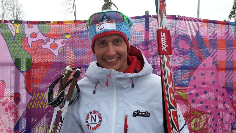 Young man holding cross-country skies smiling to the camera