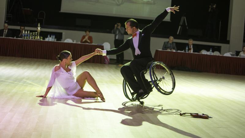 Couple on the dance floow. He is in a wheelchar, she is sitting on the floor, both pose