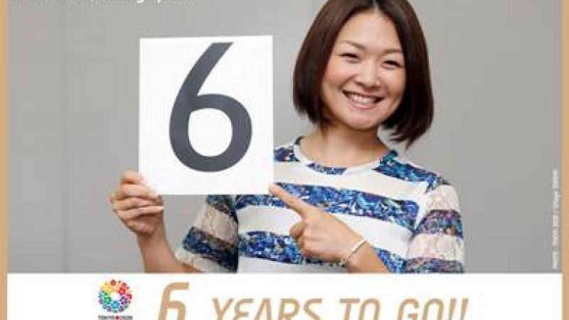Smiling women holds card with the number six to the camera. Text under the picture says 6 years to go!