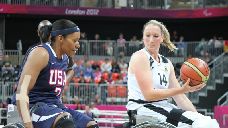 Two women in wheelchairs, playing basketball, fighting for the ball