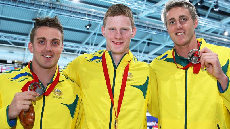 Three swimmers show their medals to the camera and smile
