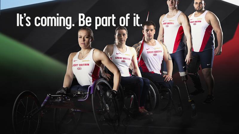 5 male and female athletes in British jerseys stand and sit (in wheelchairs) next to each others in front of a black wall. Behind them is the logo: Swansea 2014. It's coming. Be part of it. 