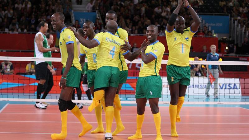 Six men celebrating on a volleyball field.
