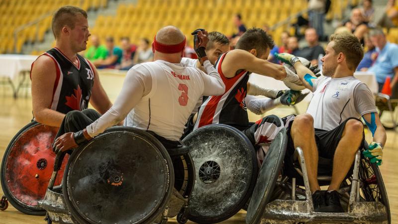 A group of four players in wheelchairs - two per side - fight for the ball during a wheelchair rugby match.