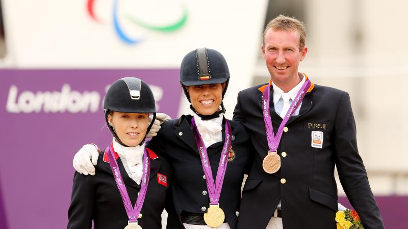 Two women and one man in dressage uniforms standing on the medals podium.