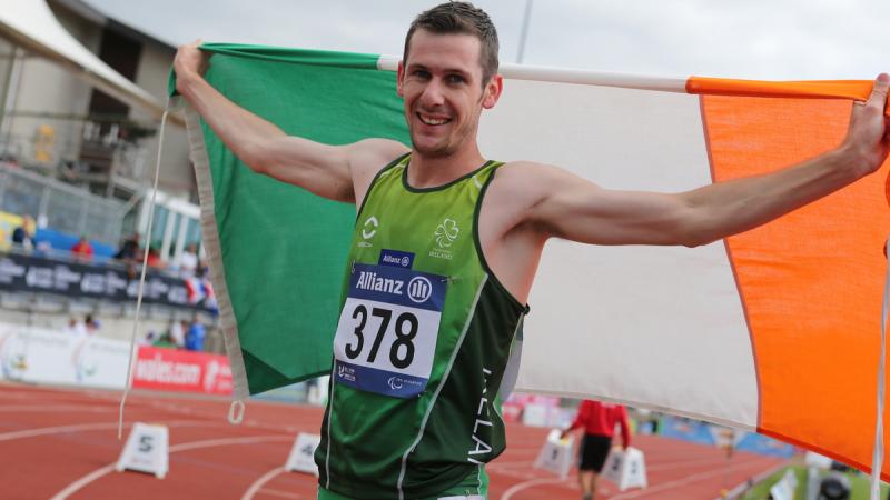 Man in green shirt holding an Irish flag and smiling to the camera