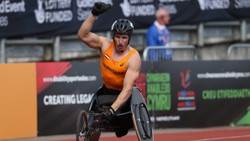 Man in racing wheelchair holding a Dutch flag, celebrating