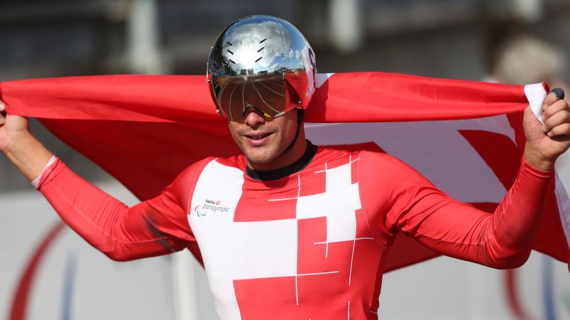 Man in red jersey with silver helmet and a Swiss flag smiling to the camera