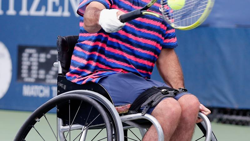 Man in wheelchair with tennis racket on the field.