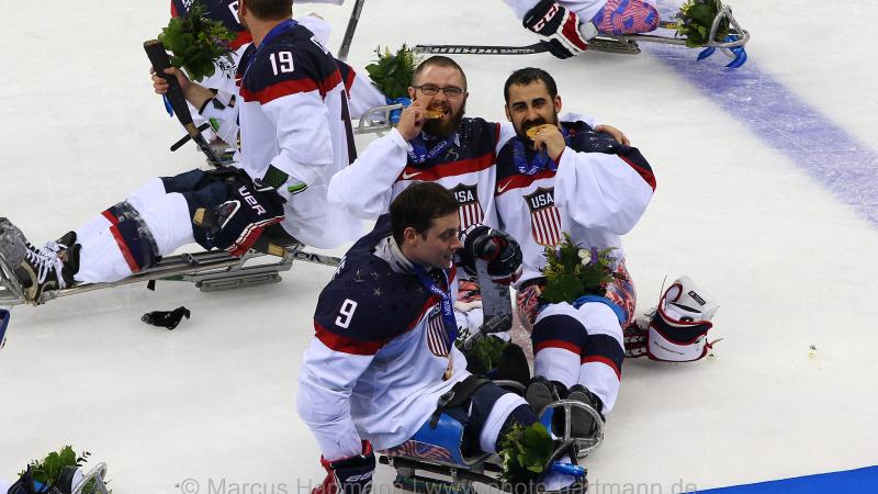 Four sledge hockey player on the ice, posing for a camera with their gold medals