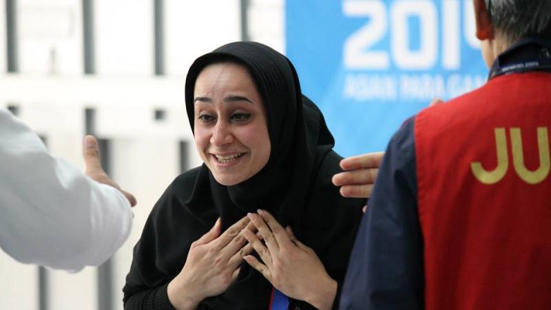 Women wearing a headscarf looks surprised and happy in front of a Incheon 2014 Asian Para Games banner