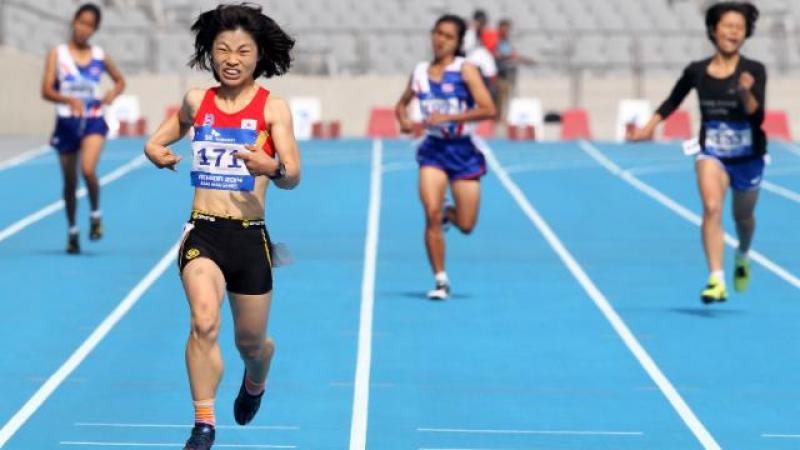 Female runner crosses the finish line on a blue track in a stadium, celebrating