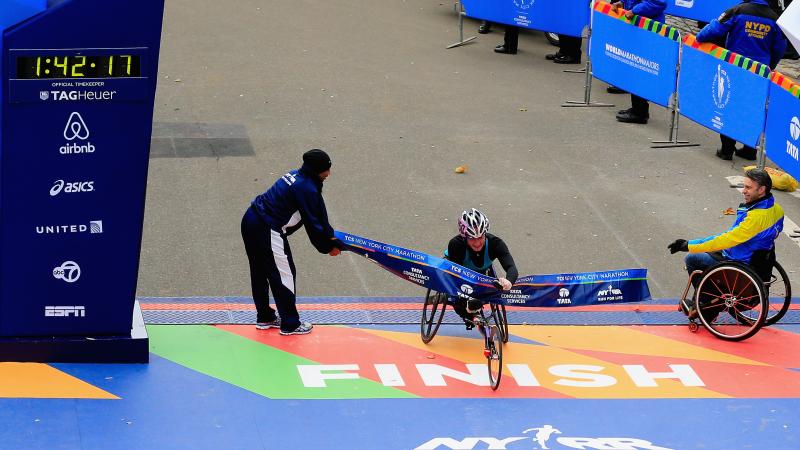 Women in racing wheelchair crosses the finish line on a street