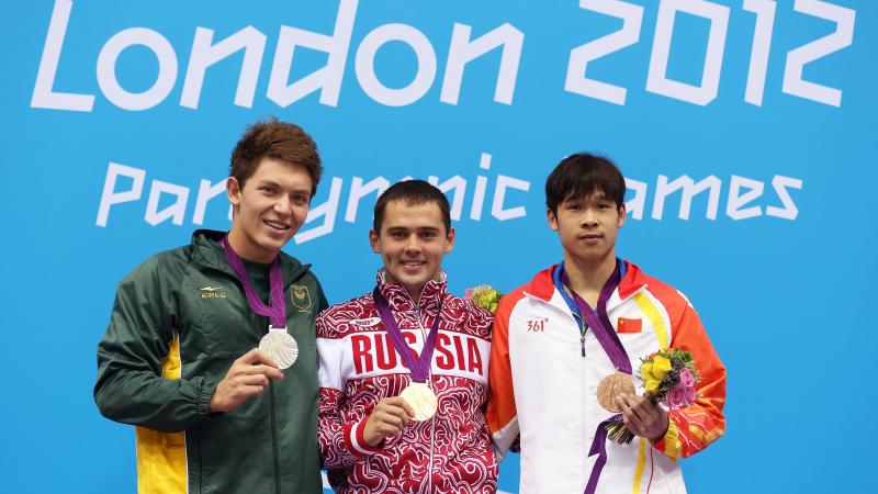 Three men on a podium, posing for the camera