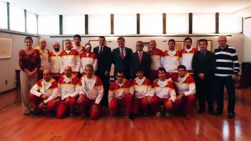 Group shot of a football team in training suits with six people in business clothes.