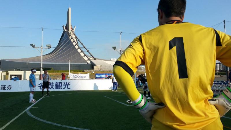 Back of a football player looking at another blindfolded player who prepares to shoot a penalty