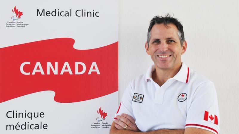 man looking at the camera with arms crossed in front of Canadian banner