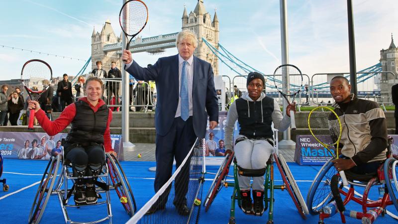 three wheelchair tennis players and the Mayor of London holding tennis rackets up in front of London Bridge