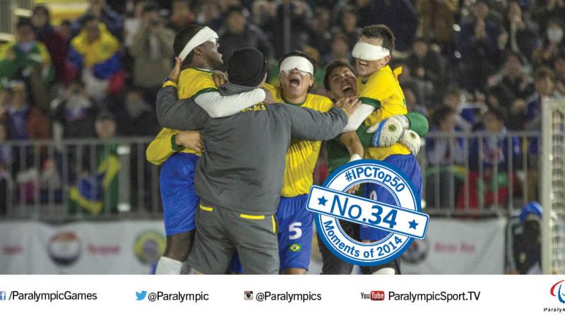 A group of five men, three blindfolded and wearing football shirts, jump up and hug in celebration