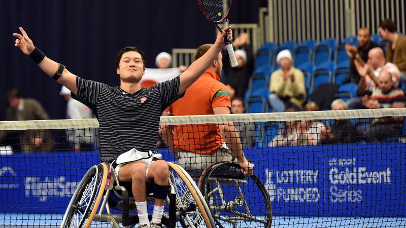 Man in wheelchair, holding tennis racket in triumphing pose