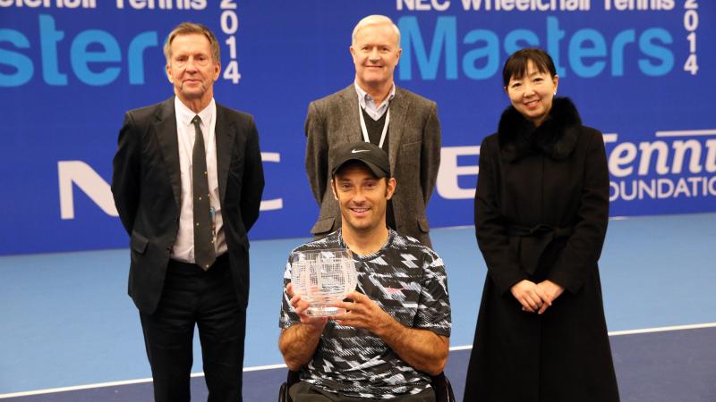 Man in wheelchair with tennis racket in triumphing pose