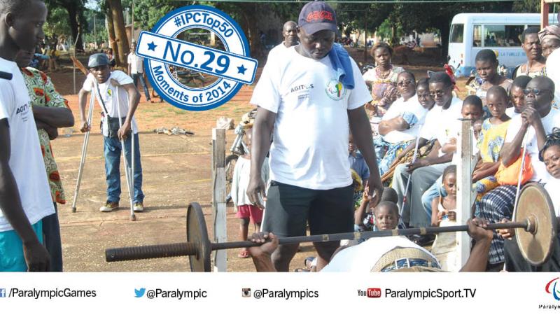 Man on bench press with other people standing around him, watching him.