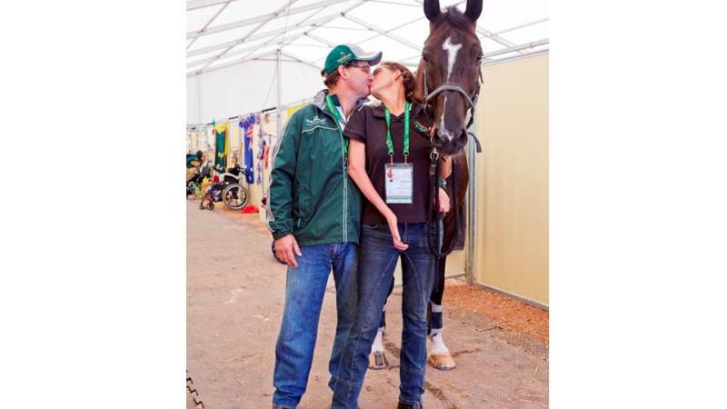 Man and women kissing, a black horse stands next to them.