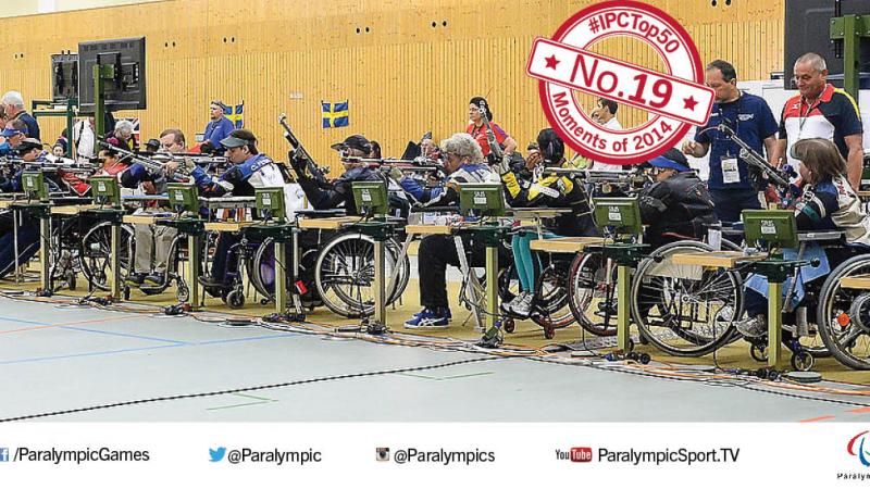 A line of seated athletes holding rifles line up for competition.