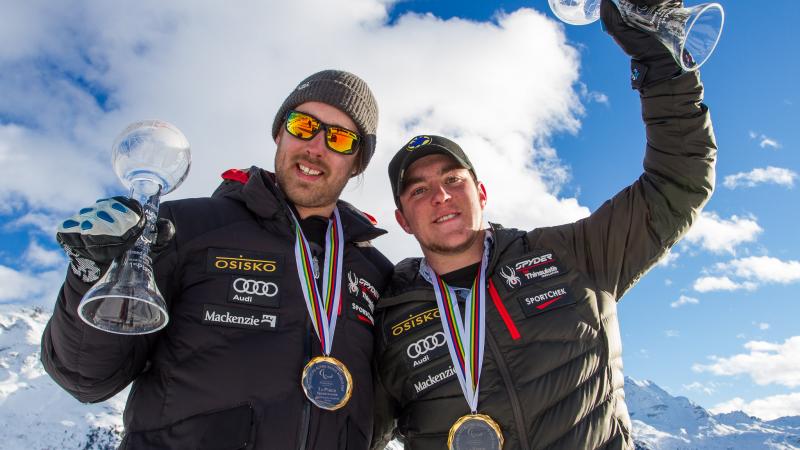 Upper bordies of two men smiling, showing their medals to the camera