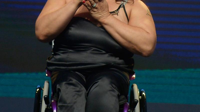 Women in black dress sitting in a wheelchair kissing a trophy