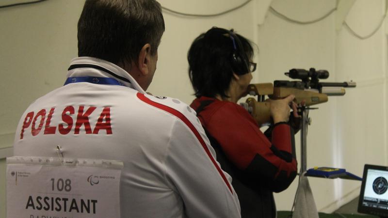 Women in a shooting range with a man standing behind her