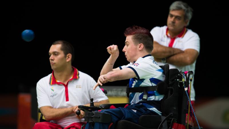 Two men in wheelchairs, one throwing a blue ball